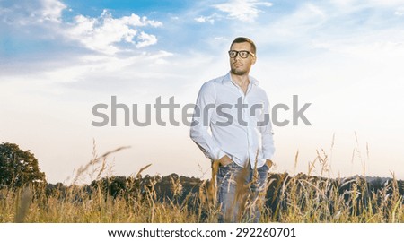 Gorgeous young man standing in a grass wearing white shirt, outdoors. Guy in nature, copyspace for text