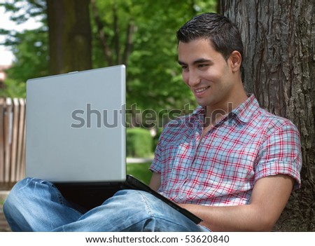 Smiling young man sitting in a forest and using a laptop
