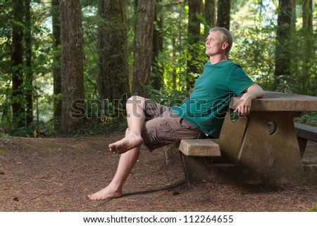 Young man sitting on a picnic bench in the woods