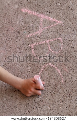 A child practices writing the alphabet on the sidewalk with pink chalk