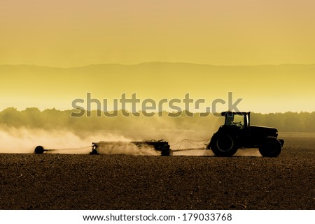 Muted, yellow, backlit silhouette of tractor raking soil