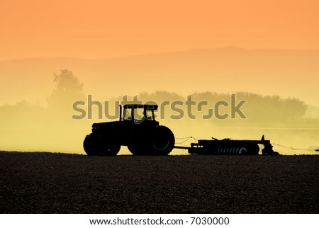 Muted Backlit Silhouette of Tractor Raking Soil