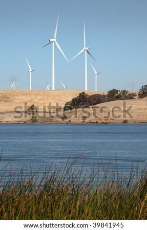 White power generating windmills under blue sky over agricultural land and Sacramento River.