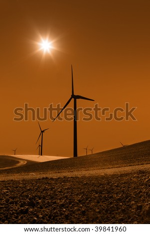 Silhouette of sepia toned power generating windmills under clear sky and recently tilled agricultural land.