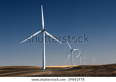 White power generating windmills under blue sky and recently tilled agricultural land.
