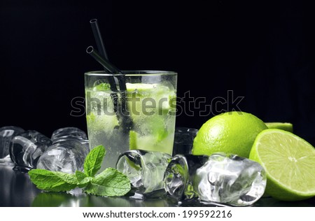 Mojito cocktail with fresh limes, mint and ice cubes on black table