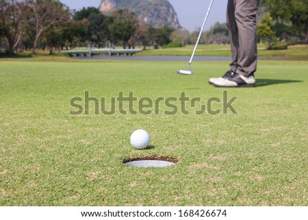 Man putting golf ball with hole