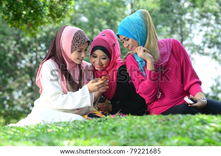 young muslim woman in head scarf meet friends and using phone in the park