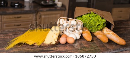 Composition of raw pasta, eggs, piece of cheese, mushrooms champignon, french bread and fresh salad lettuce on the table