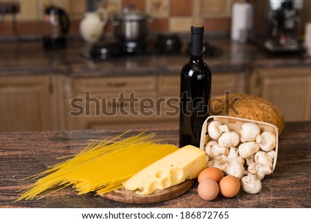 Composition of raw pasta, eggs, piece of cheese, mushrooms champignon, fresh bread and bottle of wine on the table