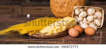 Composition of raw pasta, eggs, piece of cheese, mushrooms champignon and fresh bread on the table