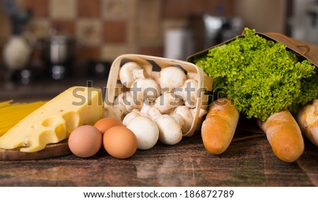Composition of raw pasta, eggs, piece of cheese, mushrooms champignon, french bread and fresh salad lettuce on the table