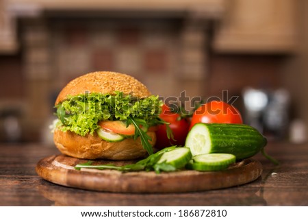 Image of home made vegetables burger with tomatoes on branch and slices of cucumber on wooden board
