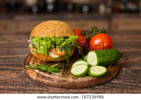 Image of home made vegetables burger with tomatoes on branch and slices of cucumber on wooden board
