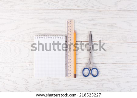 Notepad with pencil, ruler and scissors on wood table