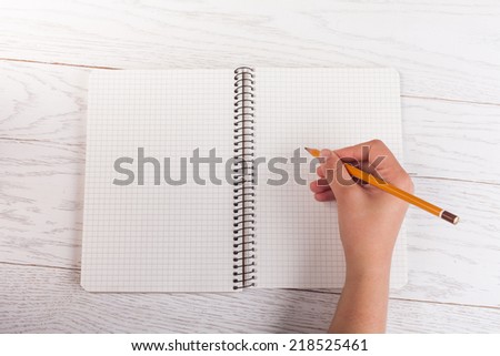 Girl hand write with pencil in notepad on wood table