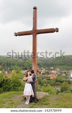 Bride and groom kissing under a wooden cross