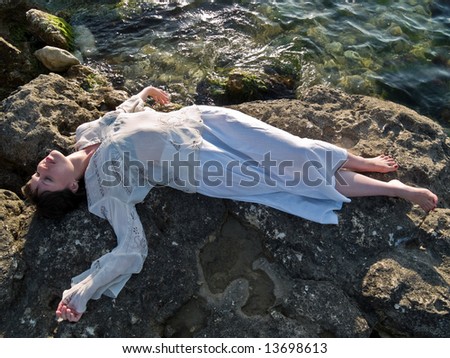 Beautiful young lady lying on sea rock ethnic dress