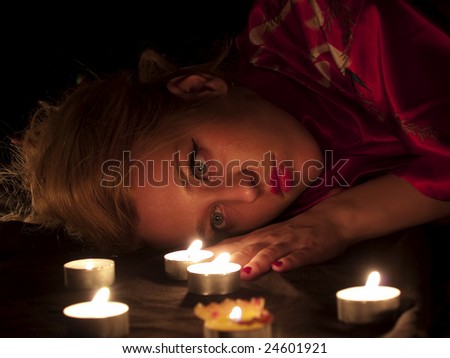 Beautiful blonde lady with oriental make-up lying in candles