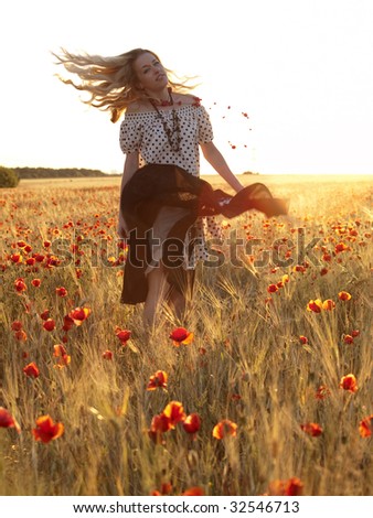 Beautiful blonde lady walking in poppy field on sunset