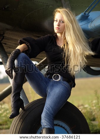 Youg blond woman sitting on vintage airplane landing gear