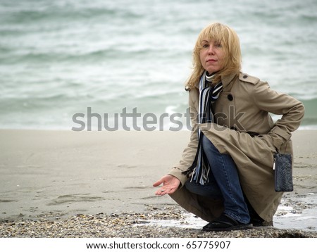 Mid-aged blonde lady sitting on sea shore autumn
