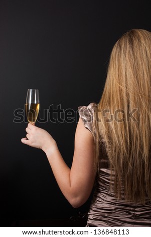 Woman in an elegant party gown from behind, hold out a champagne glass on black background