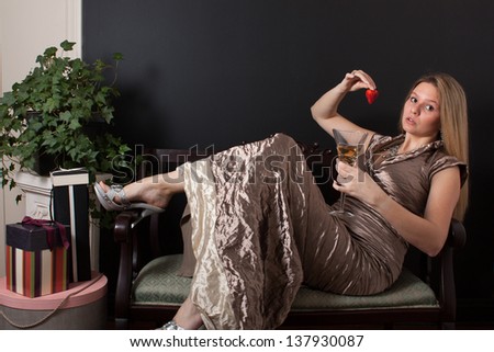 A woman in a formal gown reclines with a champagne flute and a strawberry after the party