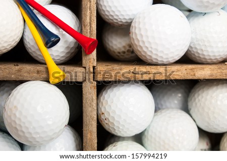 Used golf balls and colored wooden tees in a weathered antique wooden divider crate, ready for practice at the driving range.