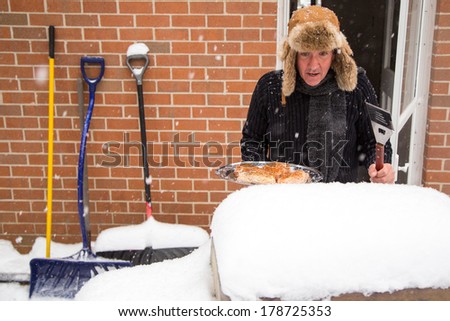 A husband heads out the back door with a tray of chicken and stares in disbelief at his barbecue buried in snow.