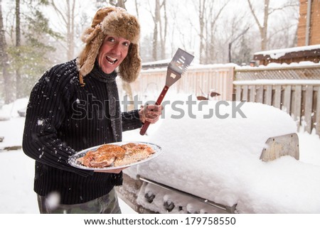 A man in a scarf and fur hat goes out in the snow to light his barbecue while the thermostat reads a chilling minus 10 degrees.  Good concept for being tired of winter and ready for a sunny vacation.