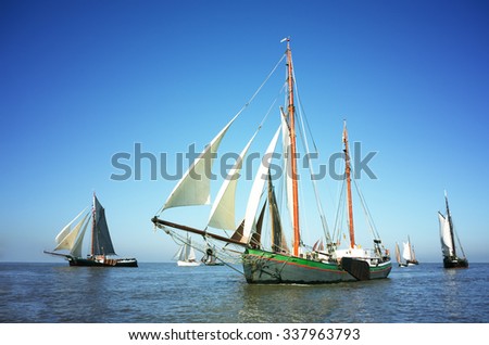 Blue color image of a fleet of traditional sailing ships on the ocean.