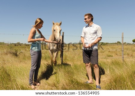 Girl and a young man feeding a horse in a meadow