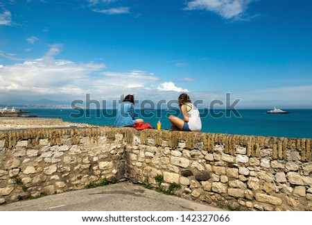 ANTIBES, FRANCE - MAY 6: Two young women relaxing on old wall and looking to Mediterranean Sea on May 6, 2013 in Antibes, France.