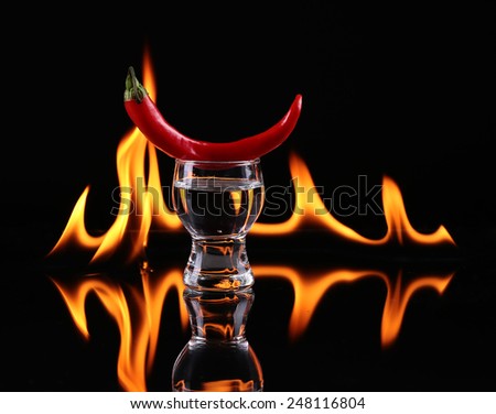 Hot chili pepper in a  shot glass with a fire on a black background
