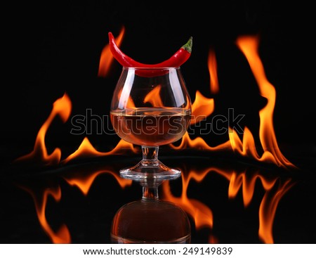 Hot chili pepper in a  cognac ballon with a fire on a black background
