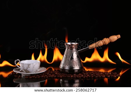 Turk and cup on coffee beans on a background of fire, black background. CONCEPT vivacity and energy