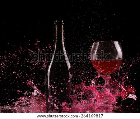 Glass and bottle of red wine splash on black