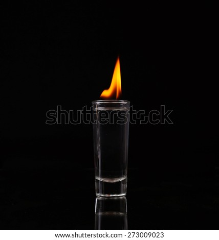 Hot chili pepper in a shot glass with a fire on a black background