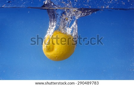 Whole lemon dropped in water against gradient blue background