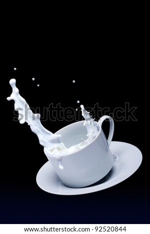 Milk spills from a cup of white color on a black background
