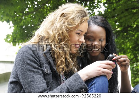 Two college friends smiling while reading a text message on a mobile phone.