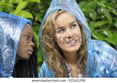 Two college friends in raincoats looking up at the rain clouds in the sky.