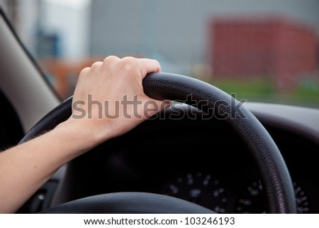 A persons hand holding steering wheel of a car.