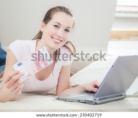 Young woman holding 10 euro while working on laptop