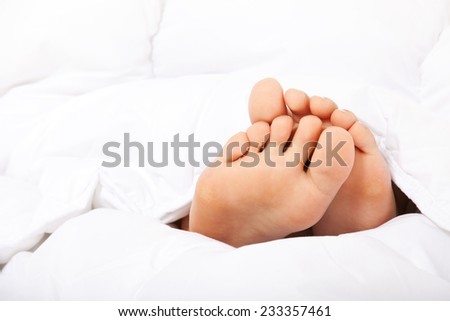 Small female feet under bed sheet.