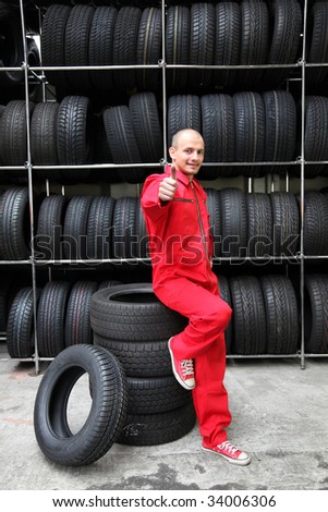 A positive mechanic in a garage standing next to a rack full of tires and making a positive gesture