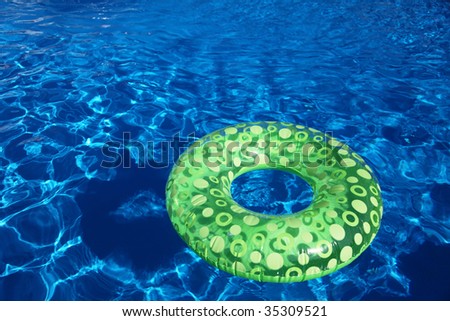 An inflatable green plastic ring swimming in a shiny blue swimming pool.