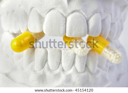A plaster cast of teeth with with a yellow pill. All on white background.