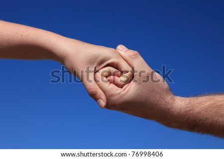Two persons holding hands in front of bright blue sky